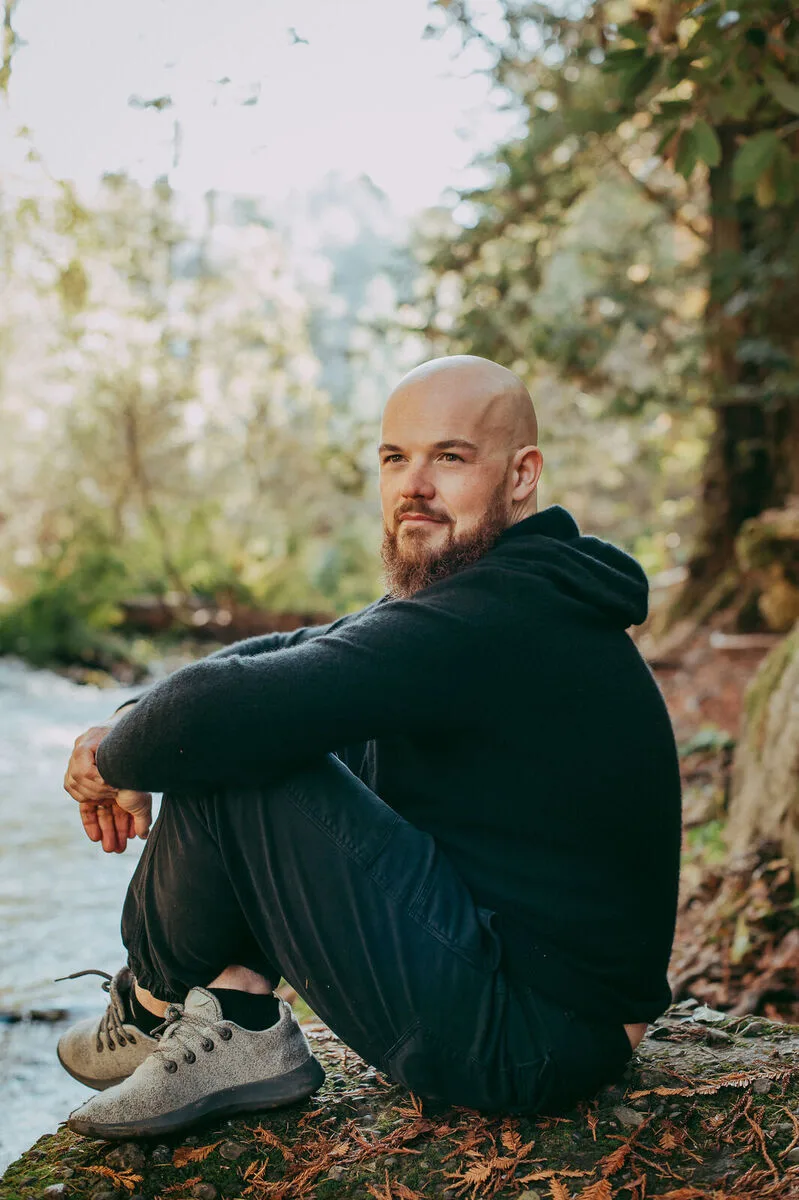 Scott Oldford sitting beside a forest stream